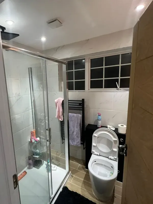 Bathroom: bath replaced with a shower, new tiles, WC and towel rail — after